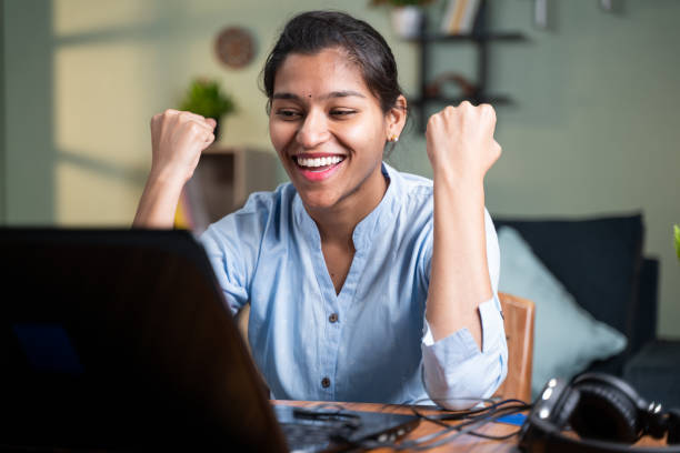 Female student expresses happiness with her hands raised after seeing her success in laptops