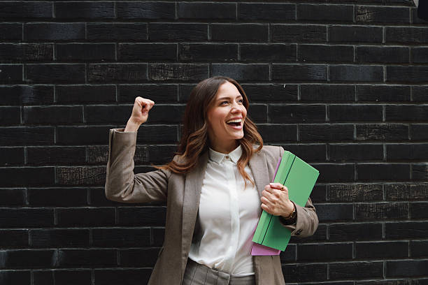 Female employee expressing happiness with the file in one hand and the other hand up on the success