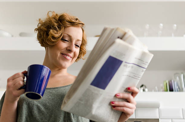 Woman drinking tea reading a cookbook article in the newspaper