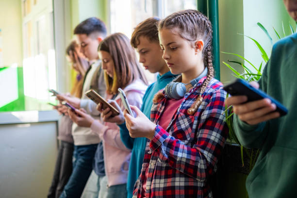 Teenage children in groups standing together and using mobile phones