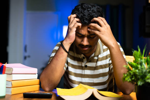 Student holding their heads in front of books as they study for competitive exams