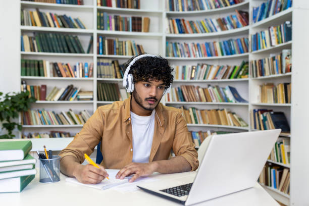 Student writing an essay after watching it from a laptop